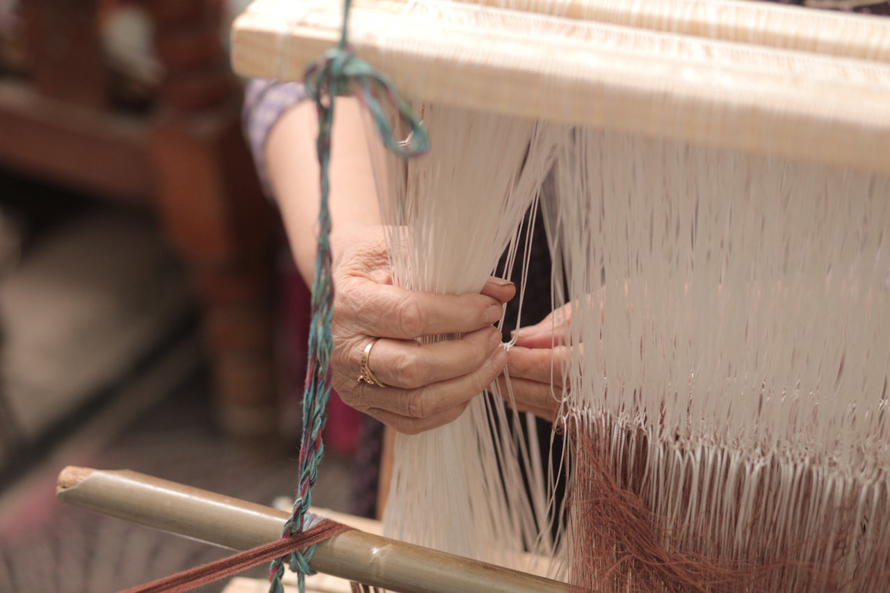 An artisan's hands tying threads on a handloom